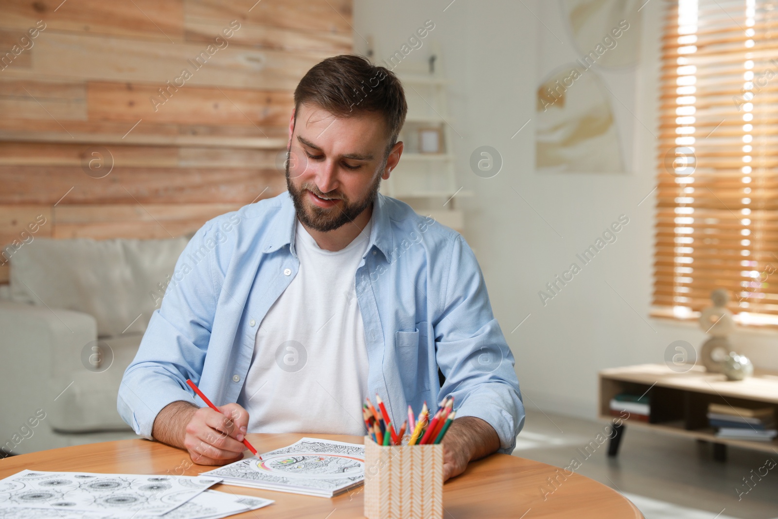 Photo of Young man coloring antistress picture at table indoors