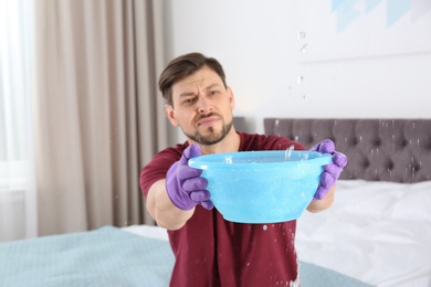 Photo of Man collecting leaking water from ceiling in bedroom. Time to call plumber