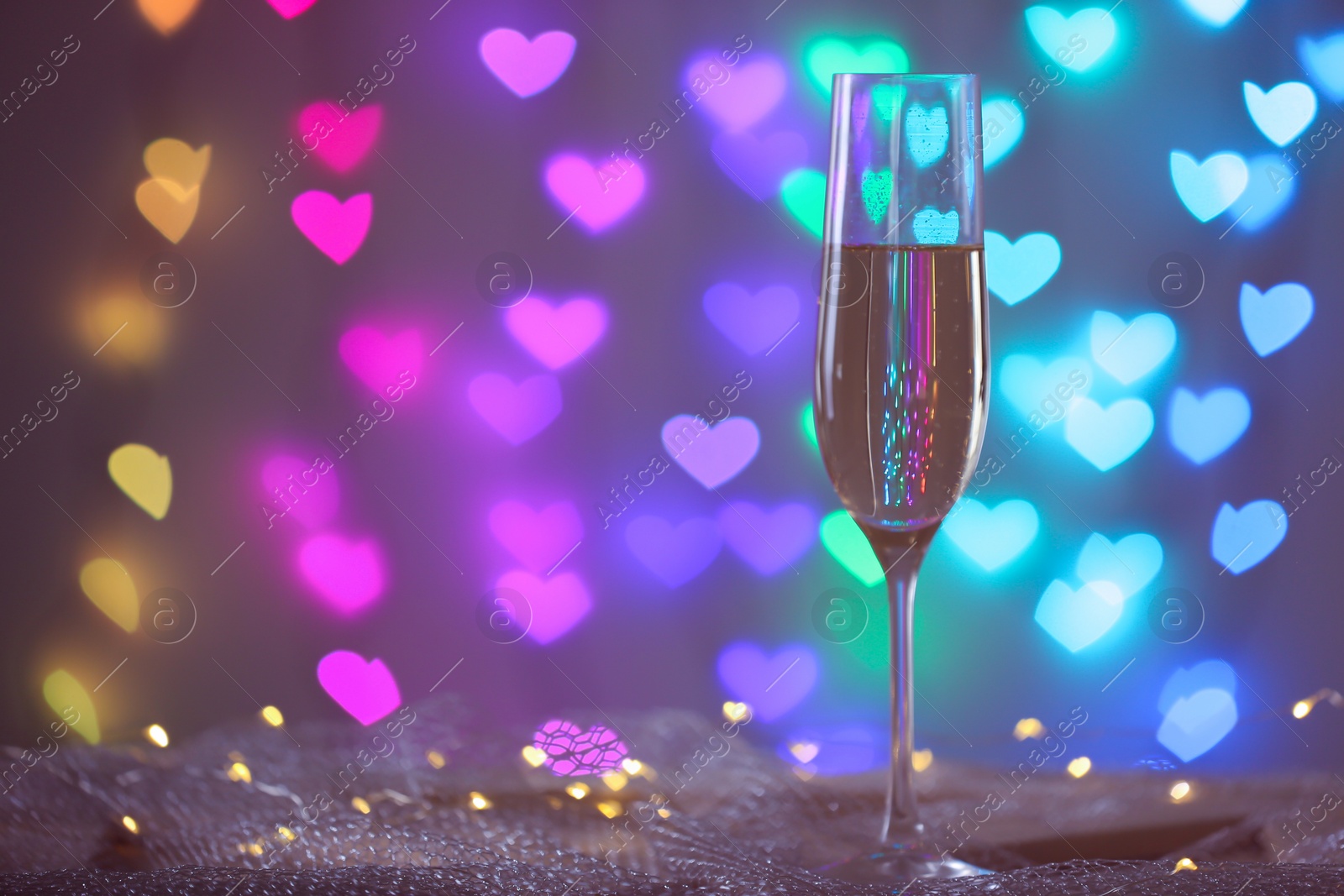 Photo of Glass of champagne on mesh fabric against blurred lights, space for text. Bokeh effect