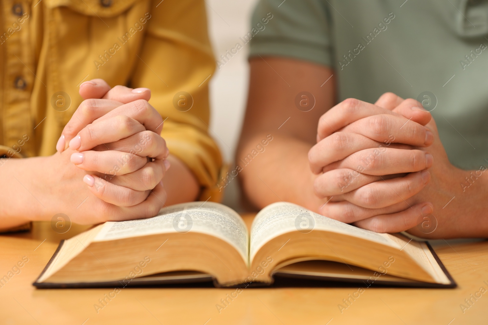 Photo of Family couple praying over Bible together at table indoors, closeup