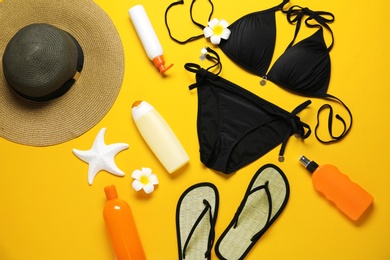 Flat lay composition with black swimsuit and beach accessories on yellow background