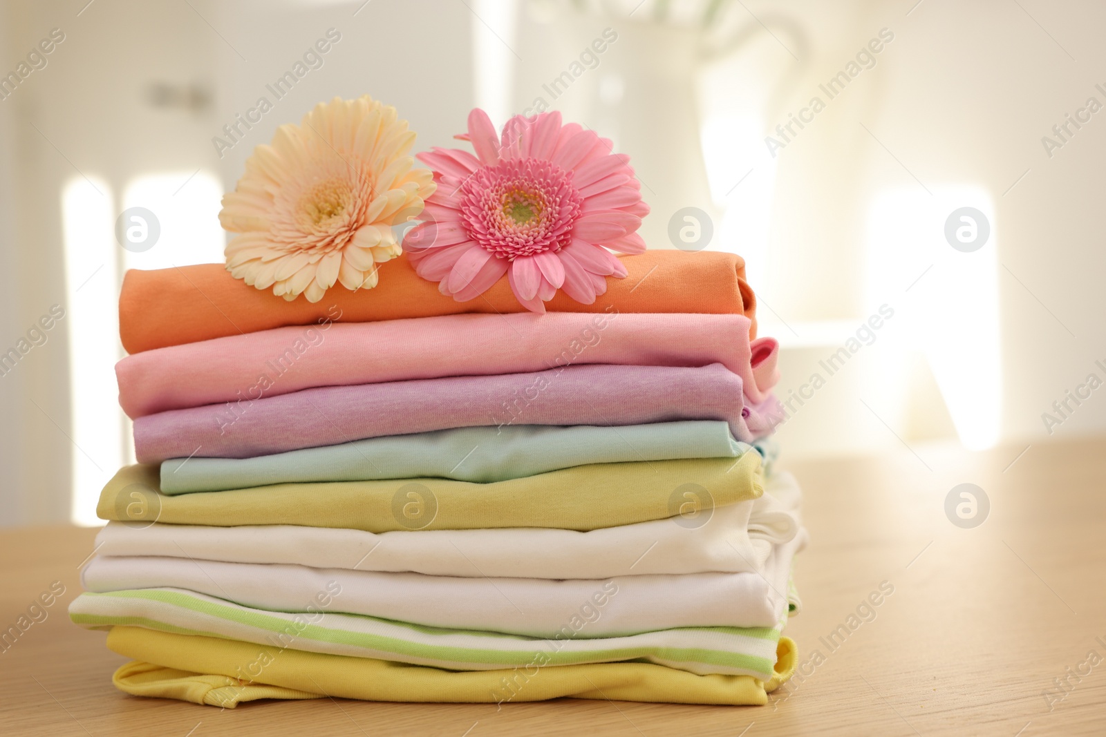 Photo of Stack of clean clothes and flowers on wooden table