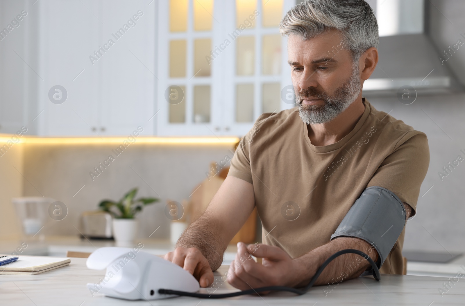 Photo of Man measuring blood pressure at table indoors