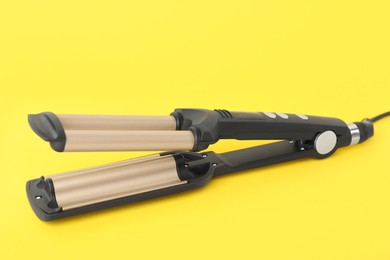 Photo of Modern triple curling iron on yellow background