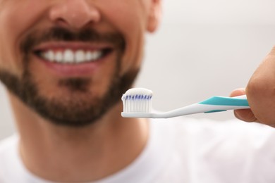 Photo of Man holding brush with toothpaste on grey background, closeup