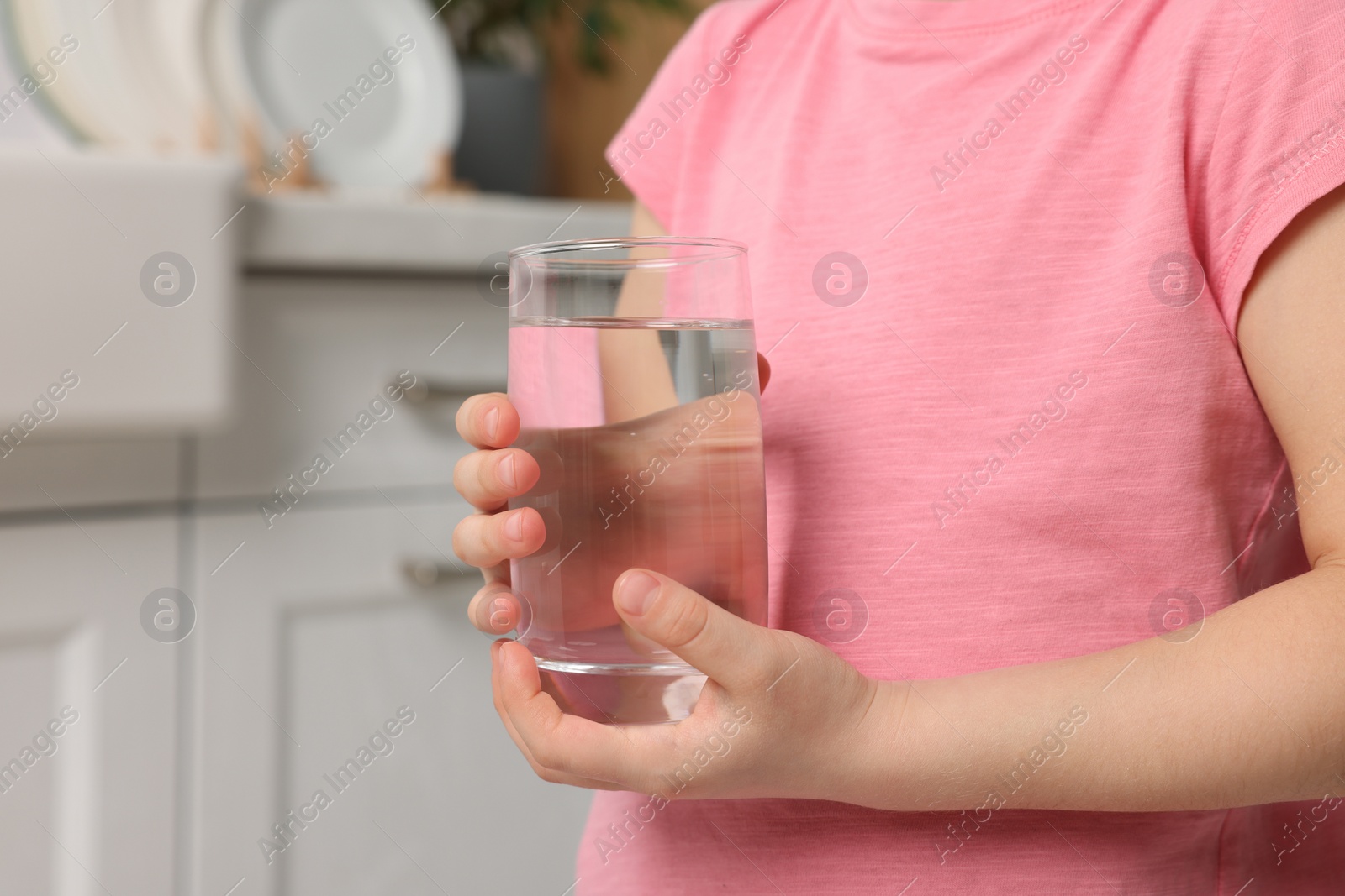 Photo of Little girl holding glass of fresh water at home, closeup