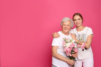 Young woman and her grandmother with flowers on pink background. Space for text