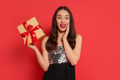 Photo of Beautiful emotional woman with Christmas gift on red background