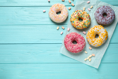 Photo of Delicious glazed donuts on blue wooden table, flat lay. Space for text