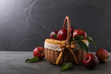 Photo of Ripe red apples and leaves in wicker basket on dark grey table. Space for text