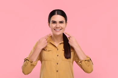 Photo of Woman pointing at her clean teeth and smiling on pink background