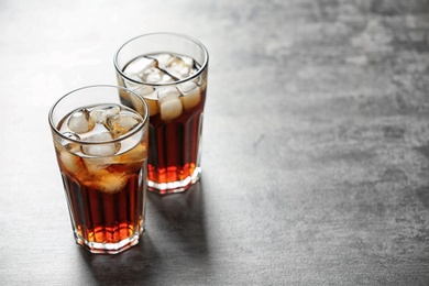 Glasses of cola with ice on grey background, space for text