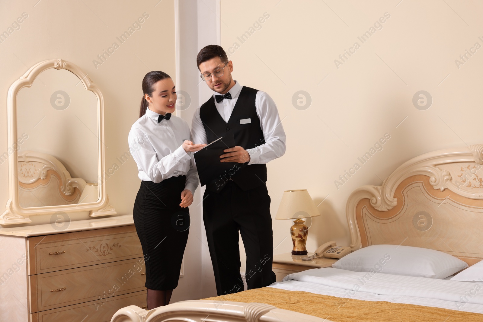 Photo of Young woman attending professional butler courses and teacher with clipboard in hotel room