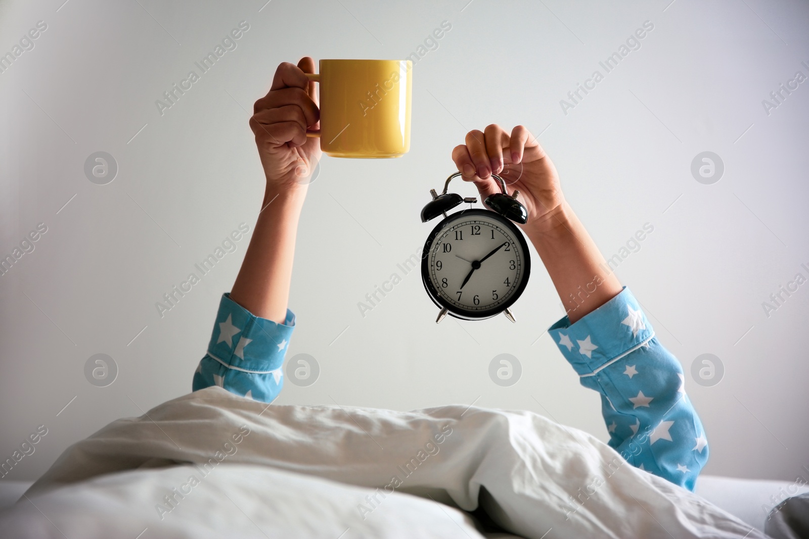 Photo of Woman with cup and alarm clock lying in bed, closeup. Morning time