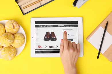 Woman with tablet shopping online on yellow background, top view