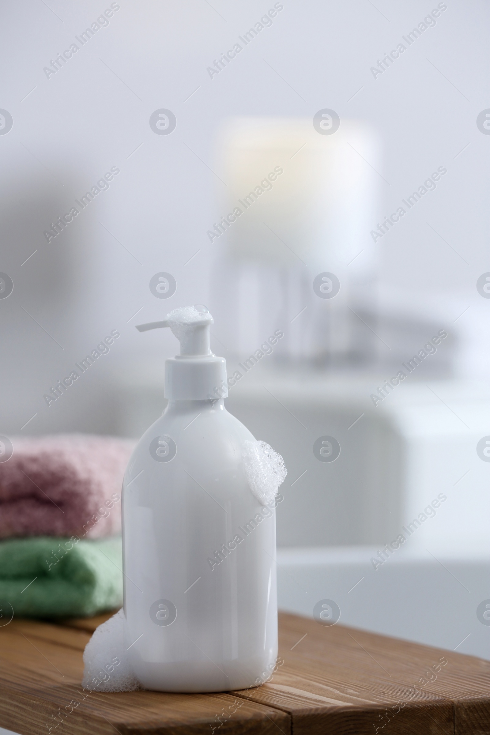 Photo of Bottle of bubble bath with foam and towels on tub in bathroom