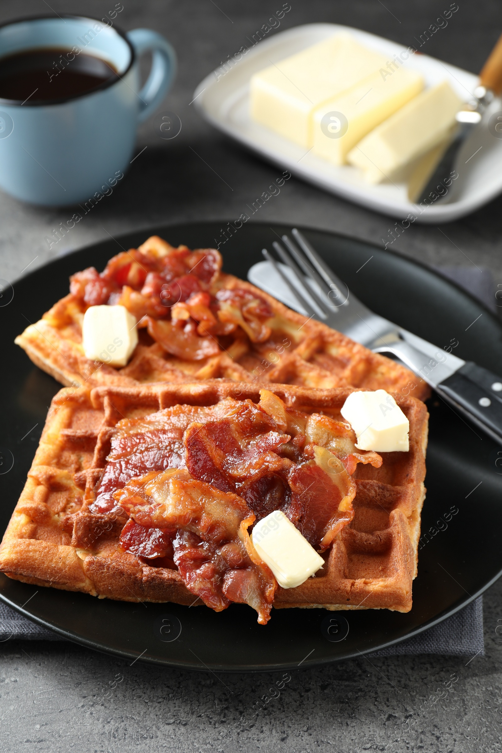 Photo of Tasty Belgian waffles served with bacon, butter and coffee on grey table, closeup