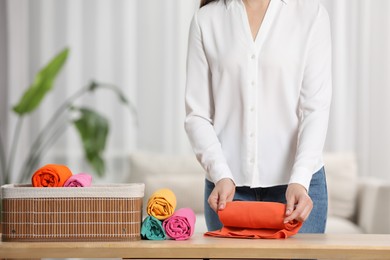 Woman rolling shirt at table indoors, closeup. Organizing clothes