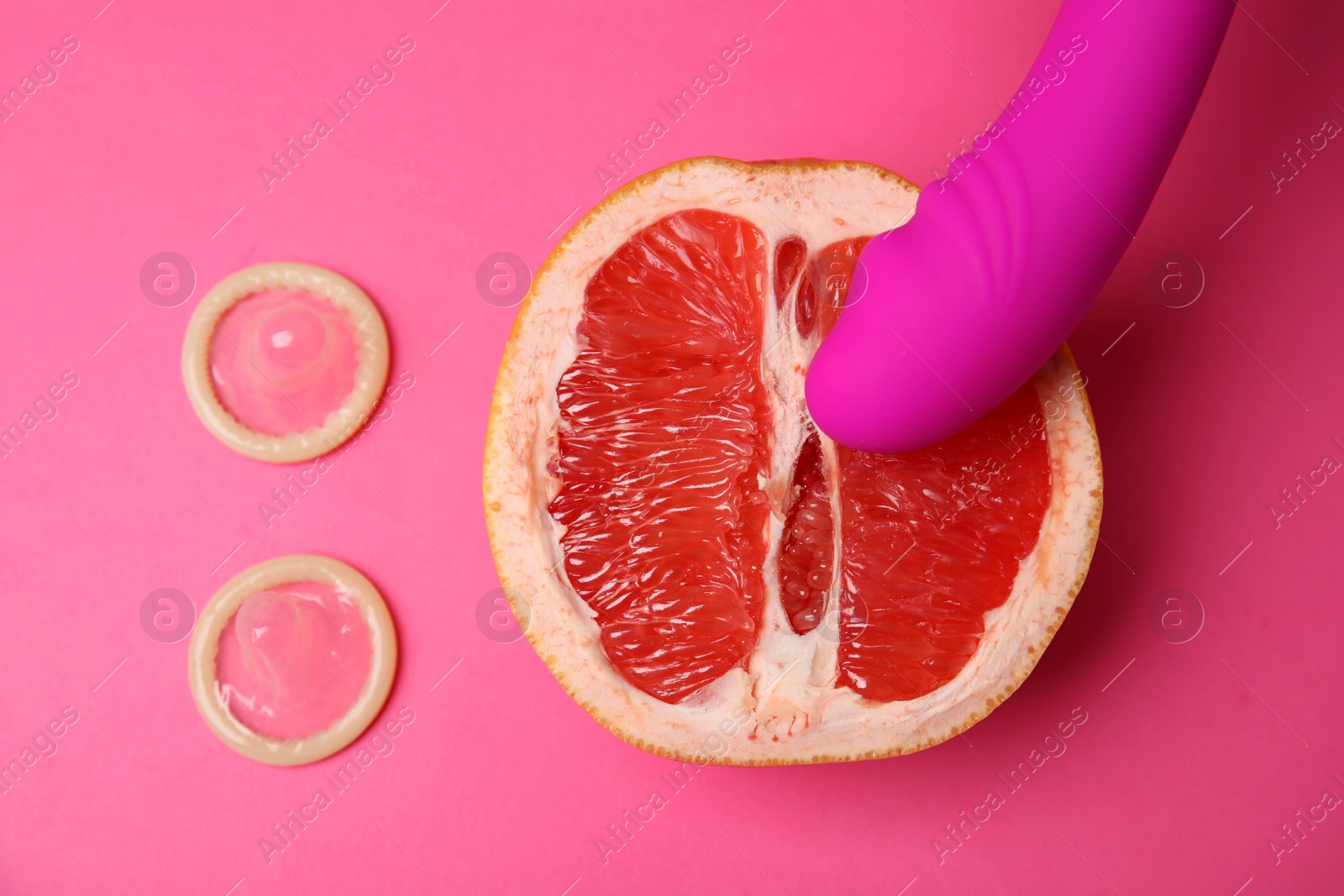 Photo of Half of grapefruit, purple vibrator and condoms on pink background, flat lay. Sex concept