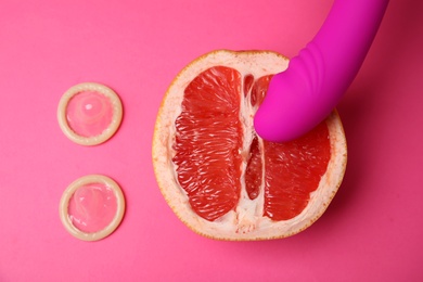 Photo of Half of grapefruit, purple vibrator and condoms on pink background, flat lay. Sex concept