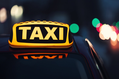 Photo of Taxi car with yellow roof sign on city street in evening, closeup