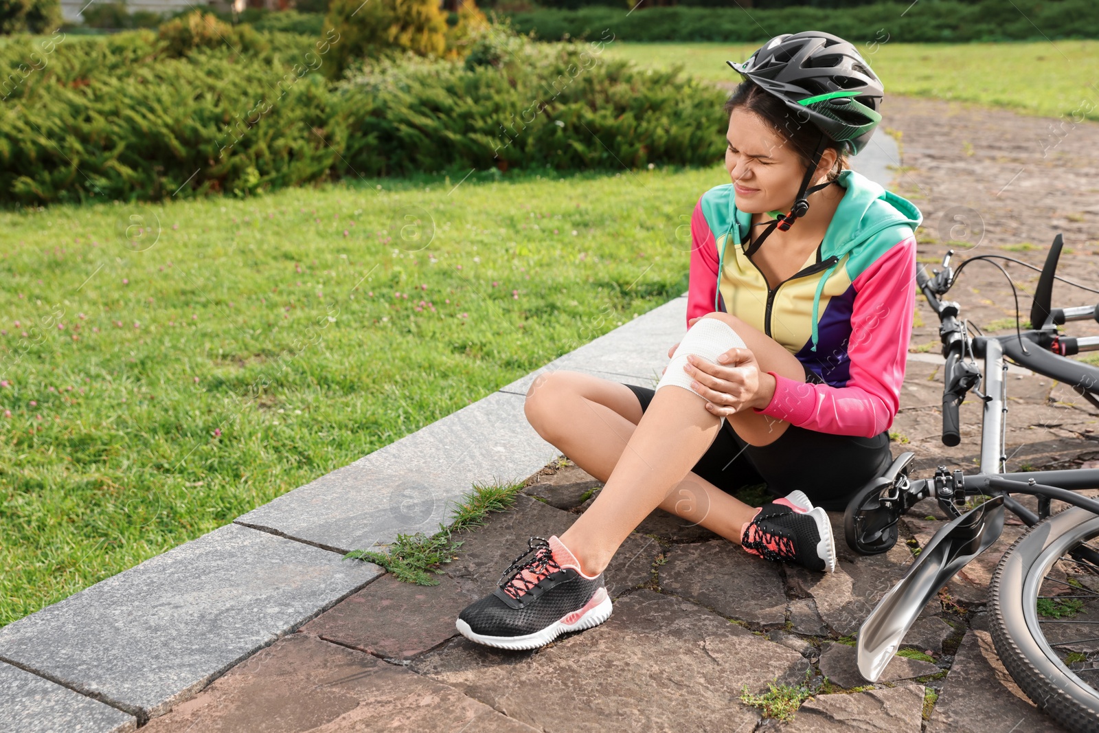 Photo of Young woman with injured knee near bicycle outdoors, space for text
