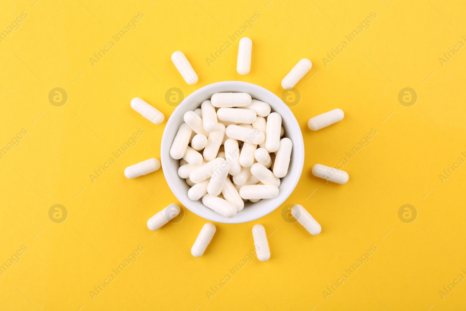 Photo of Vitamin capsules in bowl on orange background, top view