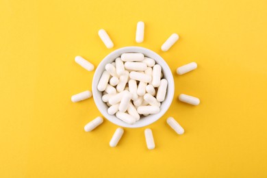 Photo of Vitamin capsules in bowl on orange background, top view