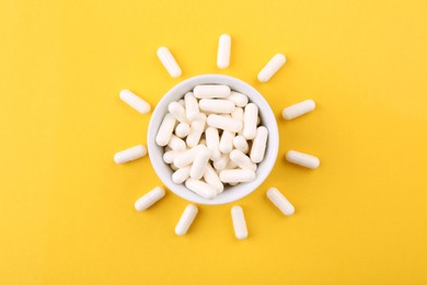 Vitamin capsules in bowl on orange background, top view