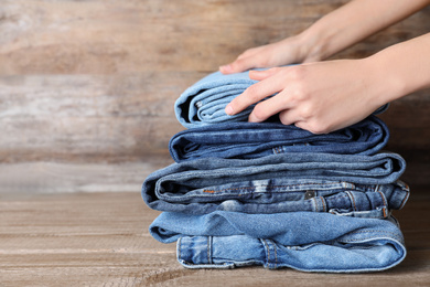 Photo of Woman folding stylish jeans on wooden table, closeup. Space for text