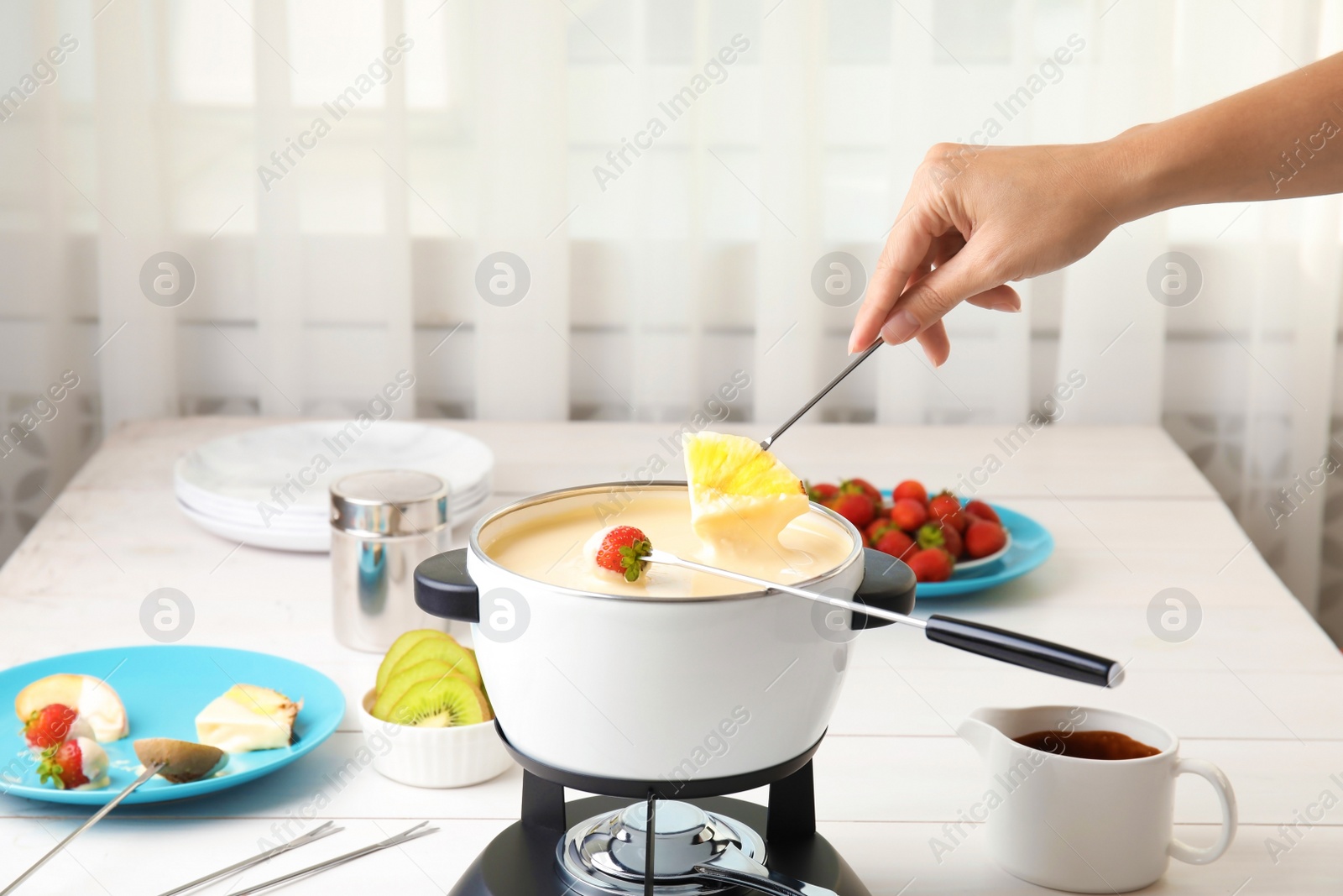 Photo of Woman dipping pineapple into pot with white chocolate fondue on table