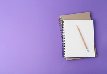 Notebooks with pencil on purple background, top view. Space for text