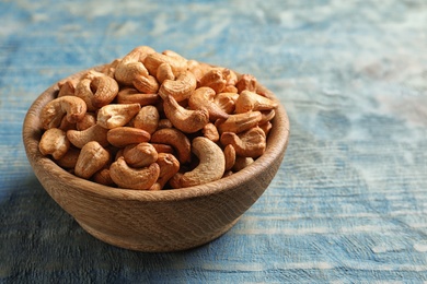 Photo of Tasty cashew nuts in bowl on wooden table. Space for text