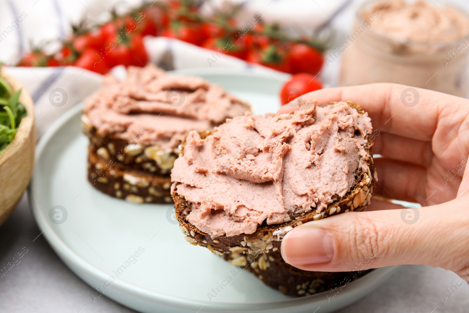 Photo of Woman holding delicious liverwurst sandwich at white table, closeup