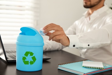 Photo of Young man throwing paper into mini recycling bin at table in office, closeup