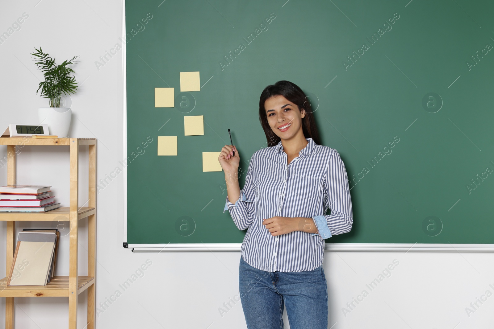 Photo of Happy young teacher giving lesson at blackboard in classroom. Space for text