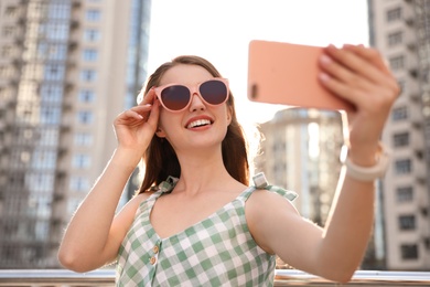 Photo of Beautiful young woman with sunglasses taking selfie outdoors