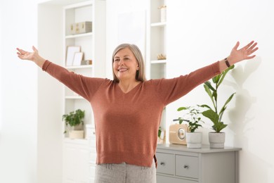Photo of Beautiful senior woman raising hands in room at home