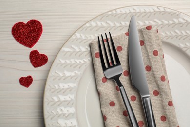 Photo of Plate with cutlery and decorative hearts on white wooden table for romantic dinner, top view