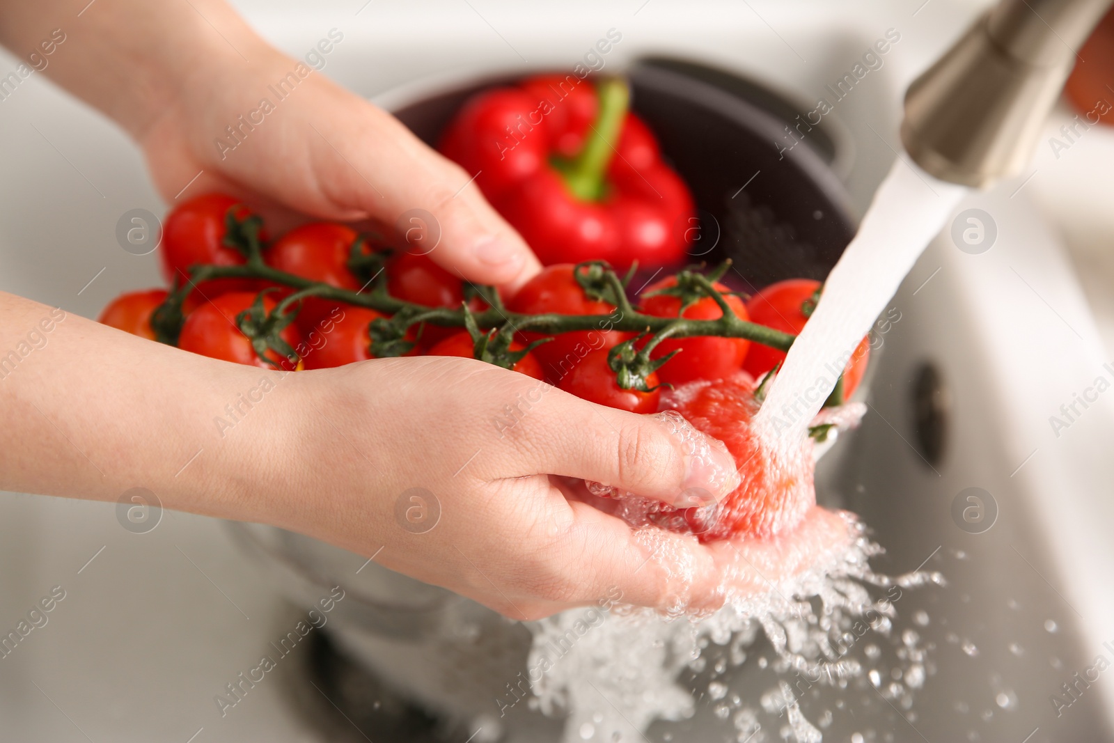 Photo of Woman washing fresh cherry tomatoes in kitchen sink, closeup