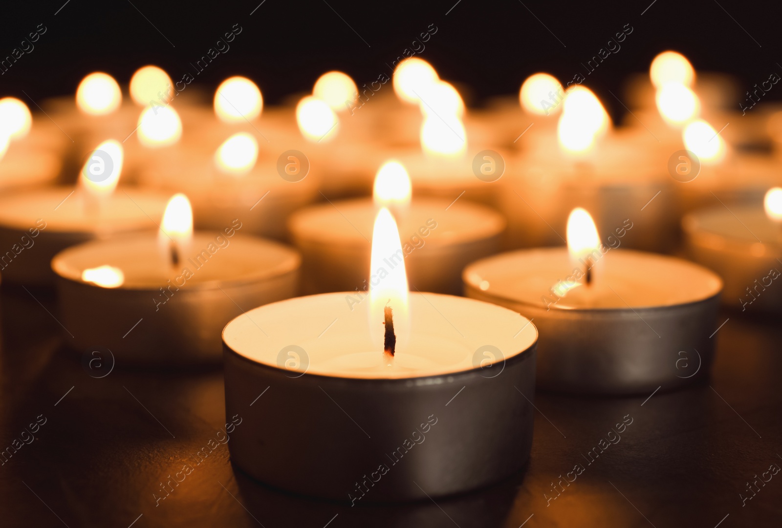 Photo of Burning candles on table in darkness, closeup. Funeral symbol