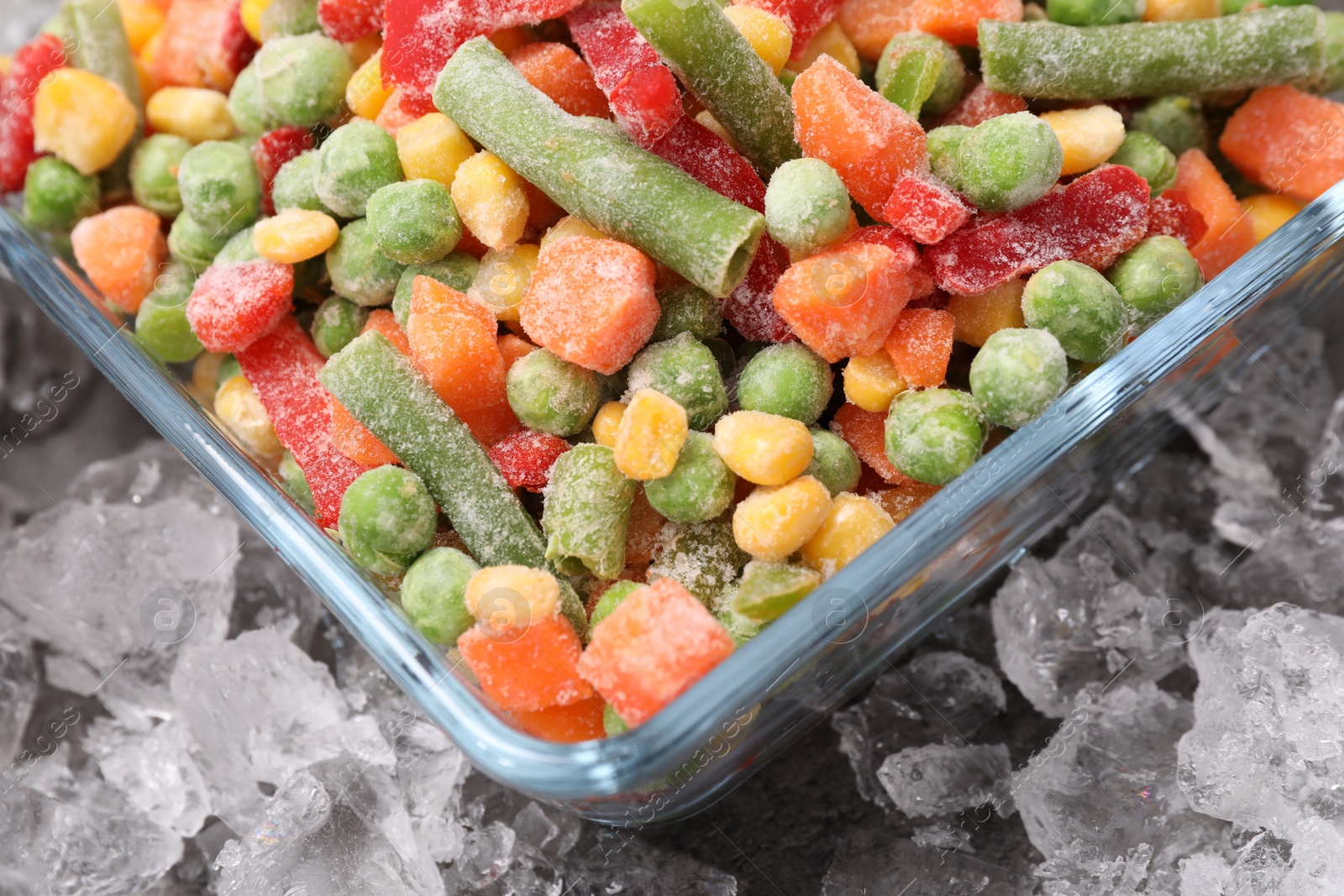 Photo of Mix of different frozen vegetables with ice on grey table, closeup