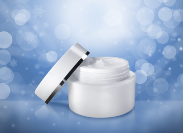 Jar of cosmetic cream on blue background with blurred snowflakes. Winter skin care