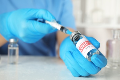 Photo of Doctor filling syringe with coronavirus vaccine at table in laboratory, closeup