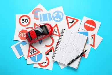 Photo of Many different road sign cards, notebook with sketch of roundabout and toy car on light blue background, flat lay. Driving school