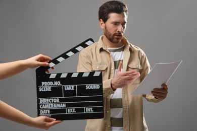 Photo of Actor performing while second assistant camera holding clapperboard on grey background