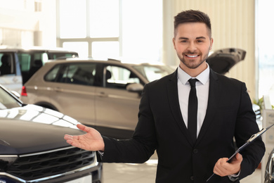 Photo of Young salesman with clipboard in modern car salon