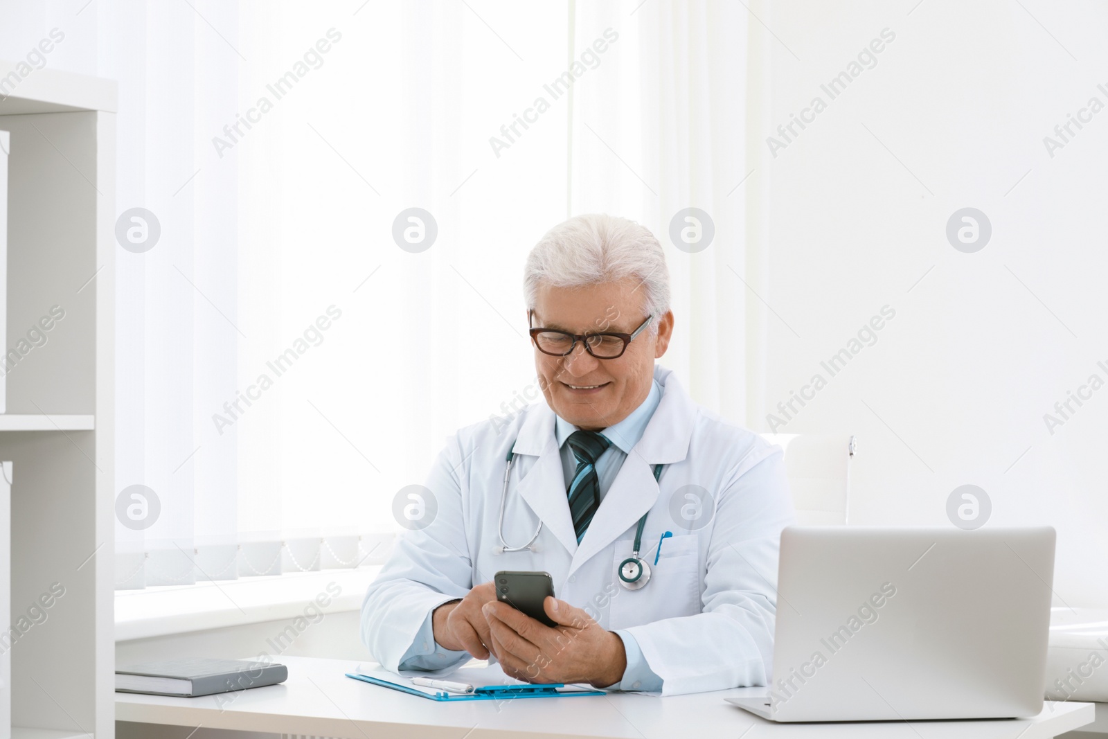 Photo of Senior doctor with smartphone at table in office