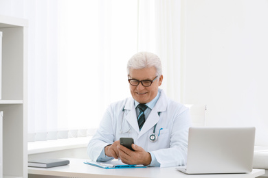 Senior doctor with smartphone at table in office