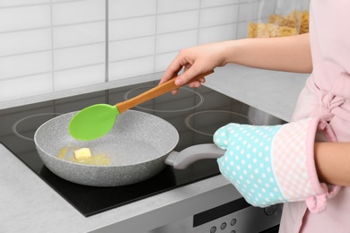 Woman stirring butter in frying pan on electric stove, closeup